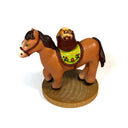 Small sculpture of a brown horse with a green, floral patterned saddle and a basket resting atop of it, holding several acorns. The sculpture stands atop of a wooden base.