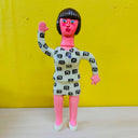 Clay sculpture of a pink woman with short black hair and bangs, wearing a matching suit coat and mini skirt outfit - white with black swirl patterning.