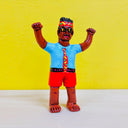 Clay sculpture of a very tan man, standing barefoot with both of his arms excitedly posed in the air. He wears shorts, a short sleeved button up, a loud patterned tie and has a matching head wrap.