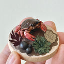 Small round wooden base with a crab sculpture held in hand against a light background