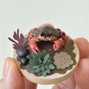 Small round wooden base with a crab sculpture held in hand against a light background