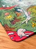 Colorful illustration on a neoprene desk mat of a dragon and fairies in a fantasy landscape with stars and flowers.