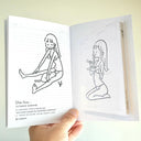 Open book with line drawings of a girl and a cat, held by a hand against a light background.