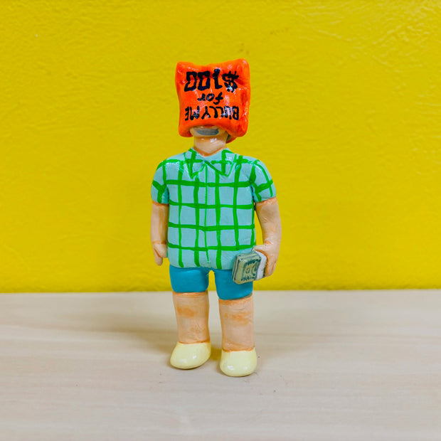 Clay sculpture of a man in blue shorts, a blue and green plaid shirt and yellow shoes. He holds a stack of money and has a bag over his head that reads "bully me for $100"