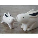 Two white wood figurines of rabbits, one is slightly larger than the other.