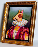 A framed whimsical painting of a dog dressed in a ruffled white collar and a pink, orange, and yellow striped outfit, set in an ornate gold frame against a light gray wall.