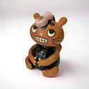 Ceramic sculpture of a brown cat-like creature with a toothy grin and looking at the top of its own head, where a character lays and wears a pink body suit.