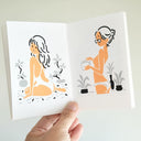 Illustrated book spread with two women, one sitting and one standing, holding a book. Both are dressed scantily and looking back over her shoulder.