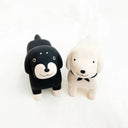 Two small dachshund dog animal figurines, side by side. One is black and the other is cream.