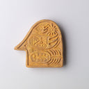 Flat tan ceramic sculpture, akin to a shaped tile or token, shaped like a bird's head with patterning on the inside of traditional folk art style shaped flowers and animals.
