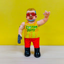 Clay sculpture of a man with short, spiky blonde hair and big red sunglasses. He holds a pistol in one hand and raises his other in a "rock on" hand shape. He wears a tank top that says "custom duty"