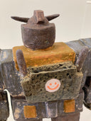 Ceramic sculpture of a Gundam with a wide, blocky body and several buttons and suit detailing with a pointed helmet.