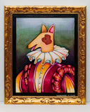 A framed whimsical painting of a dog dressed in a ruffled white collar and a pink, orange, and yellow striped outfit, set in an ornate gold frame against a light gray wall.