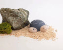 Wooden figure of a gray and white turtle with a rounded shell, flat belly and cute cartoon frown.