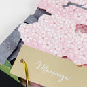 Close up of a greeting card featuring a cherry blossom design with an attached small gold "message" card.