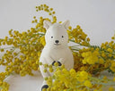 White wooden quokka figurine surrounded by yellow flowers on a light background