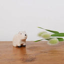 Small white animal figurine on a wooden surface with a plant in the background