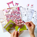 Hands assembling a paper craft with Japanese temple design andTorii gate on a white background