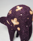 A handmade felted wool animal figure in deep purple with cream-colored shamrock and dot patterns, standing against a plain white background.