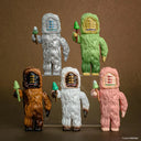 Five colorful Bigfoot figurines with different skin tones and expressions on a brown background. They all have 3 eyes and hold a skinny mushroom.