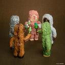 Five colorful Bigfoot figurines with different skin tones and expressions on a brown background. They all have 3 eyes and hold a skinny mushroom.
