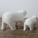 Two white wooden polar bear sculptures on a wooden surface with a light gray background