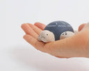 Wooden figure of a gray and white turtle with a rounded shell, flat belly and cute cartoon frown.