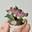 Hand holding a small decorative piece with fish and plants on a white background