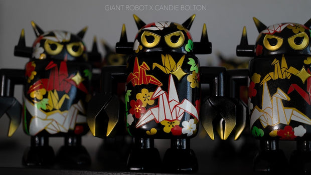 Black spray painted Big Boss Robot figures, with gold, white, red and green color accents. Their robot body features designs of paper cranes, as well as small leaf and flower iconography.