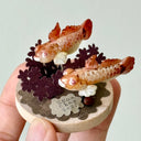 Small decorative item with two fish on a circular base held in a hand against a light background