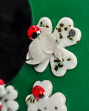 A close-up of a decorative butterfly-shaped accessory with a glossy white body and wings, dark brown speckles, and a small red-and-black ladybug attached near the upper left wing, set against a green background.