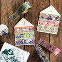Decorative washi tape rolls with house-shaped boxes on a wooden surface