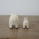 2 small white wooden figurines of pigs - one is larger than the other.