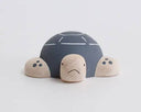 Wooden figure of a gray and white turtle with a rounded shell, flat belly and cute cartoon frown.