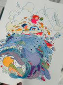 A colorful illustrated art print depicting a whimsical underwater scene with sea creatures, clouds, birds, and two children in a small boat, photographed against a light neutral background.