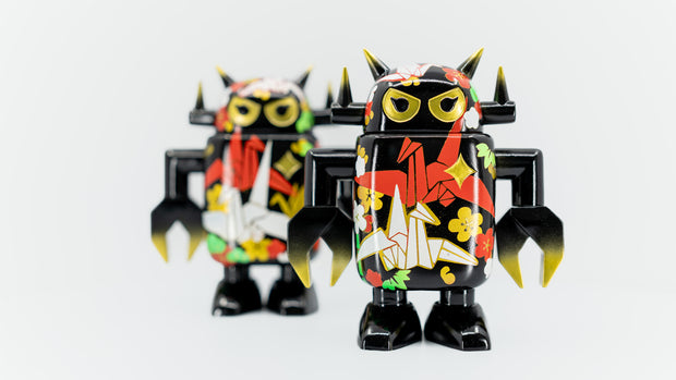 Black spray painted Big Boss Robot figures, with gold, white, red and green color accents. Their robot body features designs of paper cranes, as well as small leaf and flower iconography.