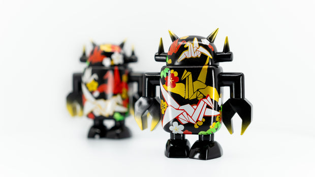 Black spray painted Big Boss Robot figures, with gold, white, red and green color accents. Their robot body features designs of paper cranes, as well as small leaf and flower iconography.