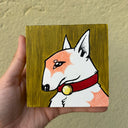 A hand holds a small square canvas painting of a stylized white and peach dog with a red collar against a mustard-yellow background, photographed against a textured beige wall.
