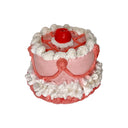Small cake figurine with pink frosting and a cherry on top against a white background