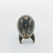 Rounded brownish silver ceramic sculpture of a quadruped with short legs and small gold eyes over a goofy open mouth smile. Its body features a subtle silver flower pattern.