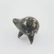 Rounded brownish silver ceramic sculpture of a quadruped with short legs and small gold eyes over a goofy open mouth smile. Its body features a subtle silver flower pattern.