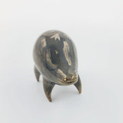 Rounded brownish silver ceramic sculpture of a quadruped with short legs and small gold eyes over a goofy open mouth smile. Its body features a subtle silver flower pattern.