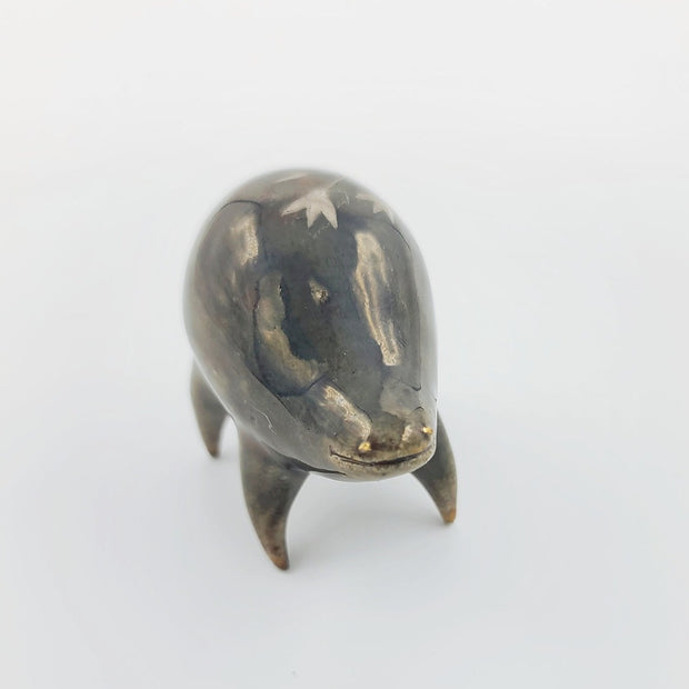 Rounded brownish silver ceramic sculpture of a quadruped with short legs and small gold eyes over a goofy open mouth smile. Its body features a subtle silver flower pattern.