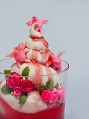 Sculpture of a ice cream sundae in a cup with strawberry syrup. It has small sculpted roses that decorate it and small pink winged creatures.