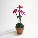 Sculpture of pinkish purple orchids coming out of a small pot. The inside of the flowers are tiny winged creatures, looking up.
