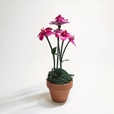 Sculpture of pinkish purple orchids coming out of a small pot. The inside of the flowers are tiny winged creatures, looking up.