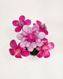 Sculpture of pinkish purple orchids coming out of a small pot. The inside of the flowers are tiny winged creatures, looking up.