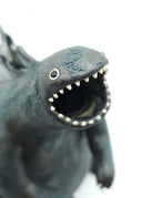 Ceramic sculpture of a large dark gray Godzilla character with a thicker, large body and a curled tail. It has gray glazed spikes along its back and has its mouth open wide, showing small sharp white teeth.