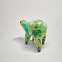 Needle felted wool sculpture of a green rounded body quadruped creature with a cute smile and small black dot eyes. Its body has patterns of clouds, water, and flowers like its a miniature world.
