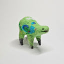 Needle felted wool sculpture of a green rounded body quadruped creature with a cute smile and small black dot eyes. Its body has patterns of clouds, water, and flowers like its a miniature world.
